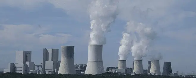 A group of cooling towers with smoke coming out.