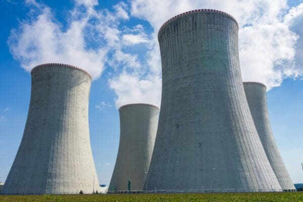 A group of three large cooling towers near grass.